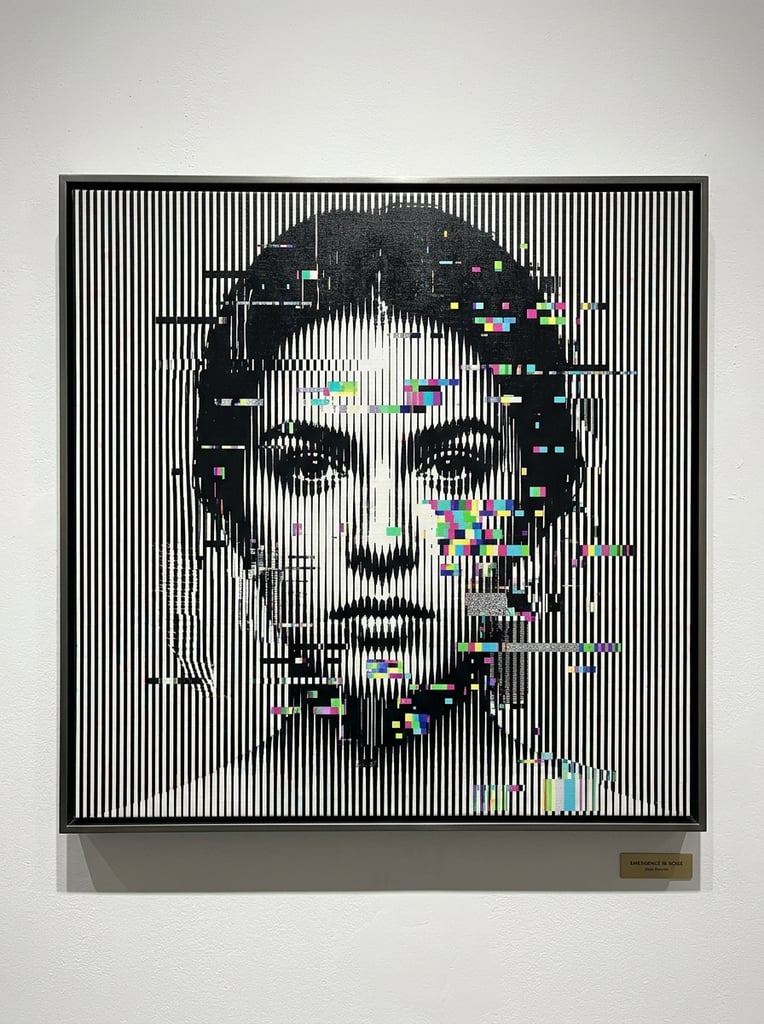 A shadowy human face emerges from a dense optical illusion of vertical black and white lines. The stark stripes are heavily fractured by digital noise and scattered rectangular RGB pixel glitches in cyan, magenta, and green. The varying density and fragmentation of the patterned lines form the contours of a person with dark hair and a neutral forward gaze. The artwork is presented as a flat canvas mounted on a stark white wall with a subtle drop shadow along its bottom edge.