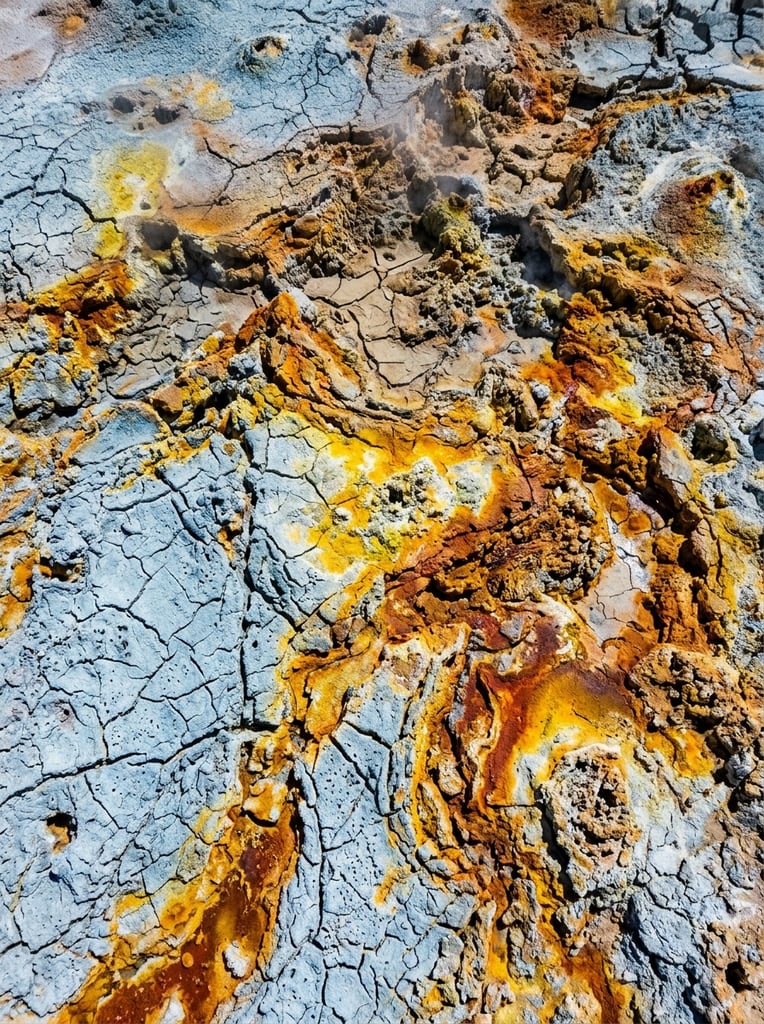 cracked pale blue crust, vivid sulfur yellow and rust orange mineral deposits, rugged porous textures, natural abstract aerial topography, sharp high-contrast photography
