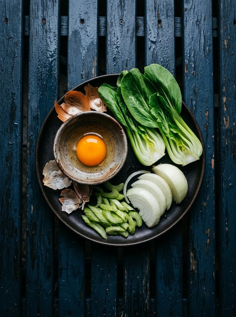 flat lay of raw ingredients on a dark plate, bright orange egg yolk in a small rustic bowl, vibrant green halved bok choy, sliced onions, celery, scattered dry skins, wet dark blue slatted wood background, moody dark food photography, top-down perspective, high contrast